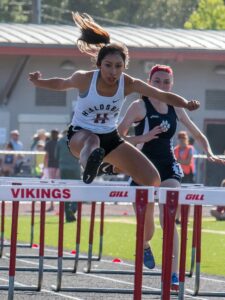 Athlete prepares for pole vault on a track with others watching.