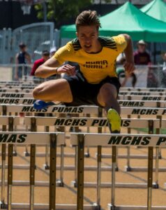 Athlete prepares for pole vault on a track with others watching.