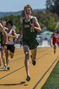 Athlete prepares for pole vault on a track with others watching.
