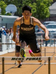 Athlete prepares for pole vault on a track with others watching.