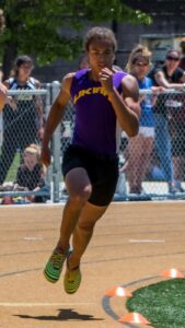 Athlete prepares for pole vault on a track with others watching.