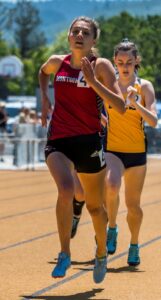 Athlete prepares for pole vault on a track with others watching.