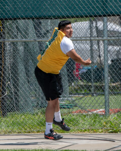 Athlete prepares for pole vault on a track with others watching.