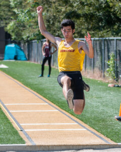 Athlete prepares for pole vault on a track with others watching.