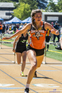 Athlete prepares for pole vault on a track with others watching.