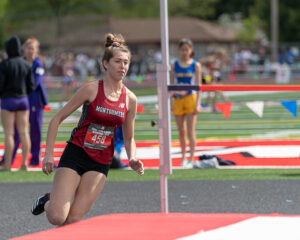 Athlete prepares for pole vault on a track with others watching.