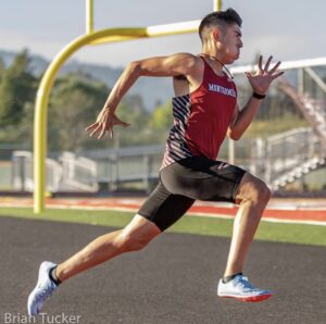 Athlete prepares for pole vault on a track with others watching.