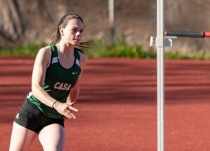 Athlete prepares for pole vault on a track with others watching.