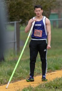 Athlete prepares for pole vault on a track with others watching.