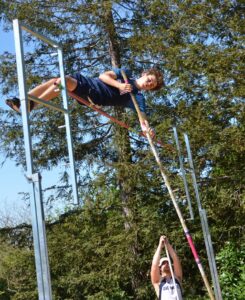 Athlete prepares for pole vault on a track with others watching.