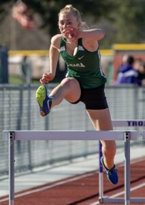 Athlete prepares for pole vault on a track with others watching.