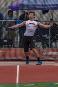 Athlete prepares for pole vault on a track with others watching.