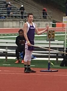 Athlete prepares for pole vault on a track with others watching.