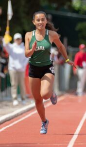 Athlete prepares for pole vault on a track with others watching.