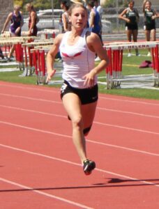 Athlete prepares for pole vault on a track with others watching.