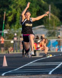 Athlete prepares for pole vault on a track with others watching.
