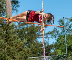 Athlete prepares for pole vault on a track with others watching.