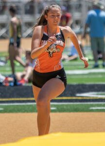 Athlete prepares for pole vault on a track with others watching.