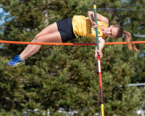 Athlete prepares for pole vault on a track with others watching.