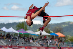 Athlete prepares for pole vault on a track with others watching.