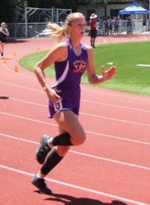 Athlete prepares for pole vault on a track with others watching.