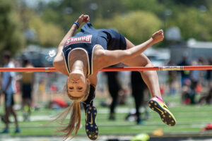 Athlete prepares for pole vault on a track with others watching.