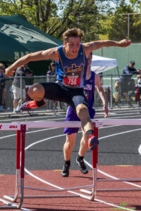 Athlete prepares for pole vault on a track with others watching.
