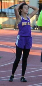 Athlete prepares for pole vault on a track with others watching.