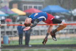 Athlete prepares for pole vault on a track with others watching.