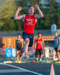 Athlete prepares for pole vault on a track with others watching.