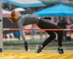 Athlete prepares for pole vault on a track with others watching.