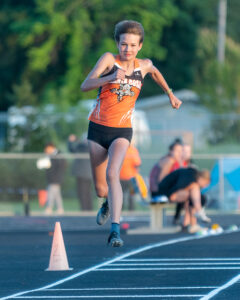 Athlete prepares for pole vault on a track with others watching.