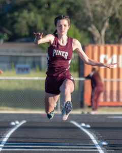 Athlete prepares for pole vault on a track with others watching.