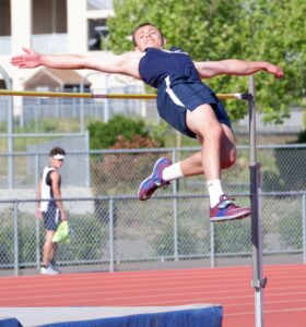Athlete prepares for pole vault on a track with others watching.