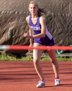 Athlete prepares for pole vault on a track with others watching.