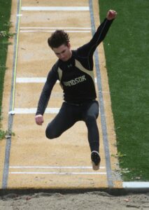 Athlete prepares for pole vault on a track with others watching.