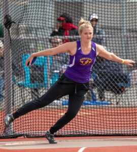 Athlete prepares for pole vault on a track with others watching.