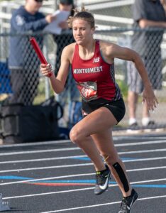 Athlete prepares for pole vault on a track with others watching.