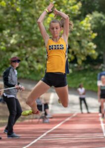 Athlete prepares for pole vault on a track with others watching.