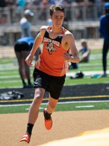 Athlete prepares for pole vault on a track with others watching.