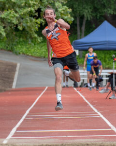 Athlete prepares for pole vault on a track with others watching.
