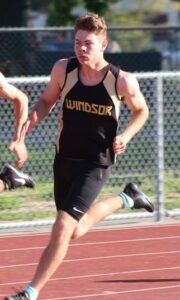 Athlete prepares for pole vault on a track with others watching.