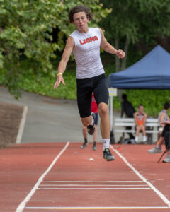Athlete prepares for pole vault on a track with others watching.