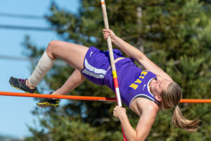 Athlete prepares for pole vault on a track with others watching.