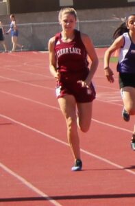 Athlete prepares for pole vault on a track with others watching.