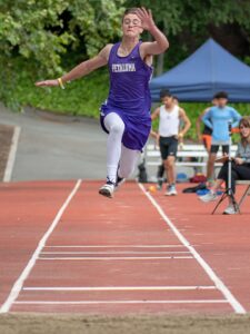 Athlete prepares for pole vault on a track with others watching.