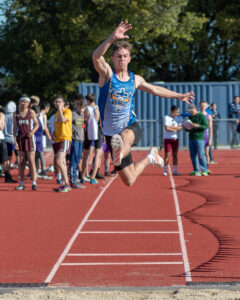 Athlete prepares for pole vault on a track with others watching.