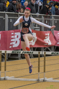 Athlete prepares for pole vault on a track with others watching.