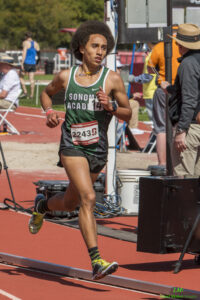 Athlete prepares for pole vault on a track with others watching.