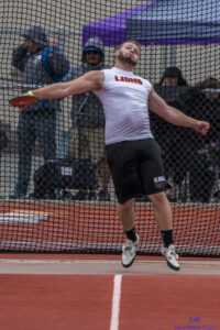 Athlete prepares for pole vault on a track with others watching.
